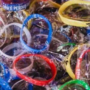 Una pila di Braccialetti in silicone nei colori rosso, blu, verde, giallo e nero, alcuni avvolti in plastica. Ogni braccialetto presenta una frase diversa stampata in bianco.